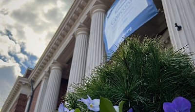 An angled photograph with a pot of flowers in the foreground and the library entrance in the background banner